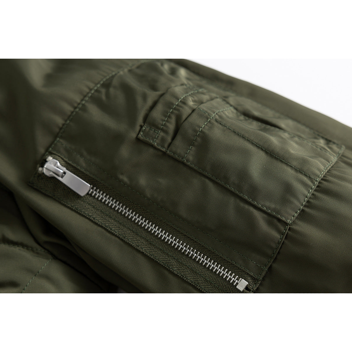Close-up of an olive bomber jacket sleeve with a zippered utility pocket and stitched flap.