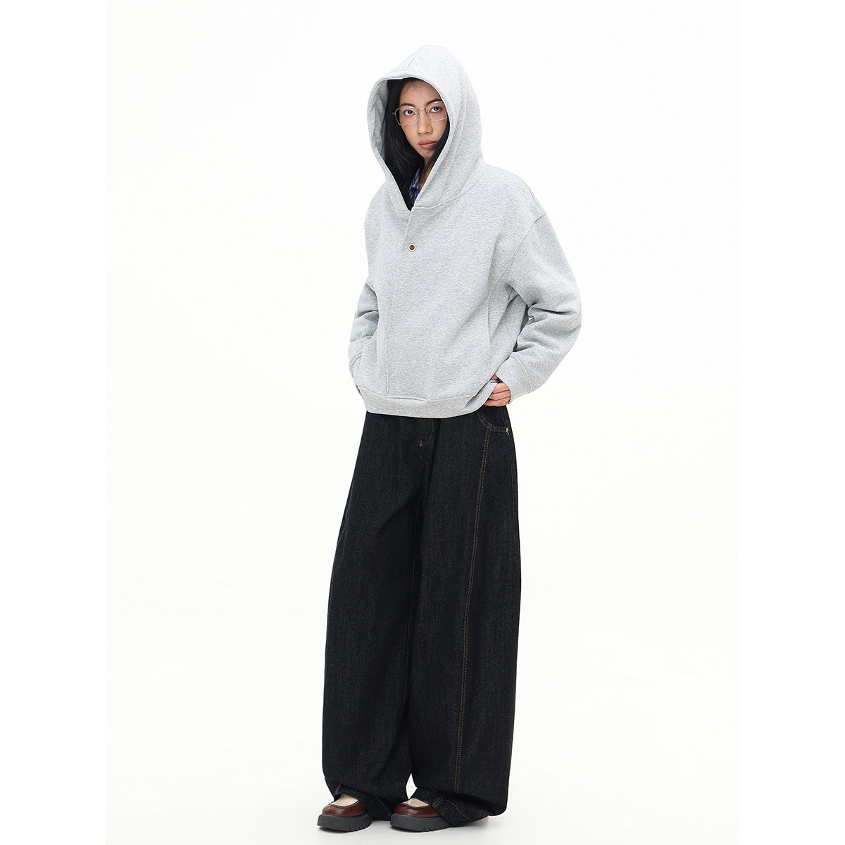 Full-length model wearing the light gray sweatshirt with its hood up, paired with dark wide-leg jeans.