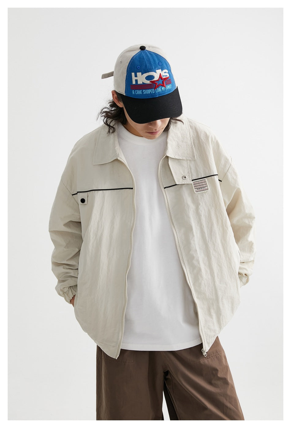 Model wearing an open ivory zip jacket with black piping and a chest patch, viewed from the front.