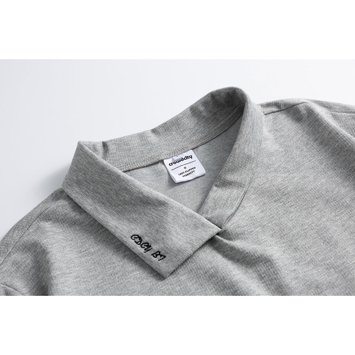 Close-up of a heather-gray crossover collar with a sewn neck label and small black embroidery.