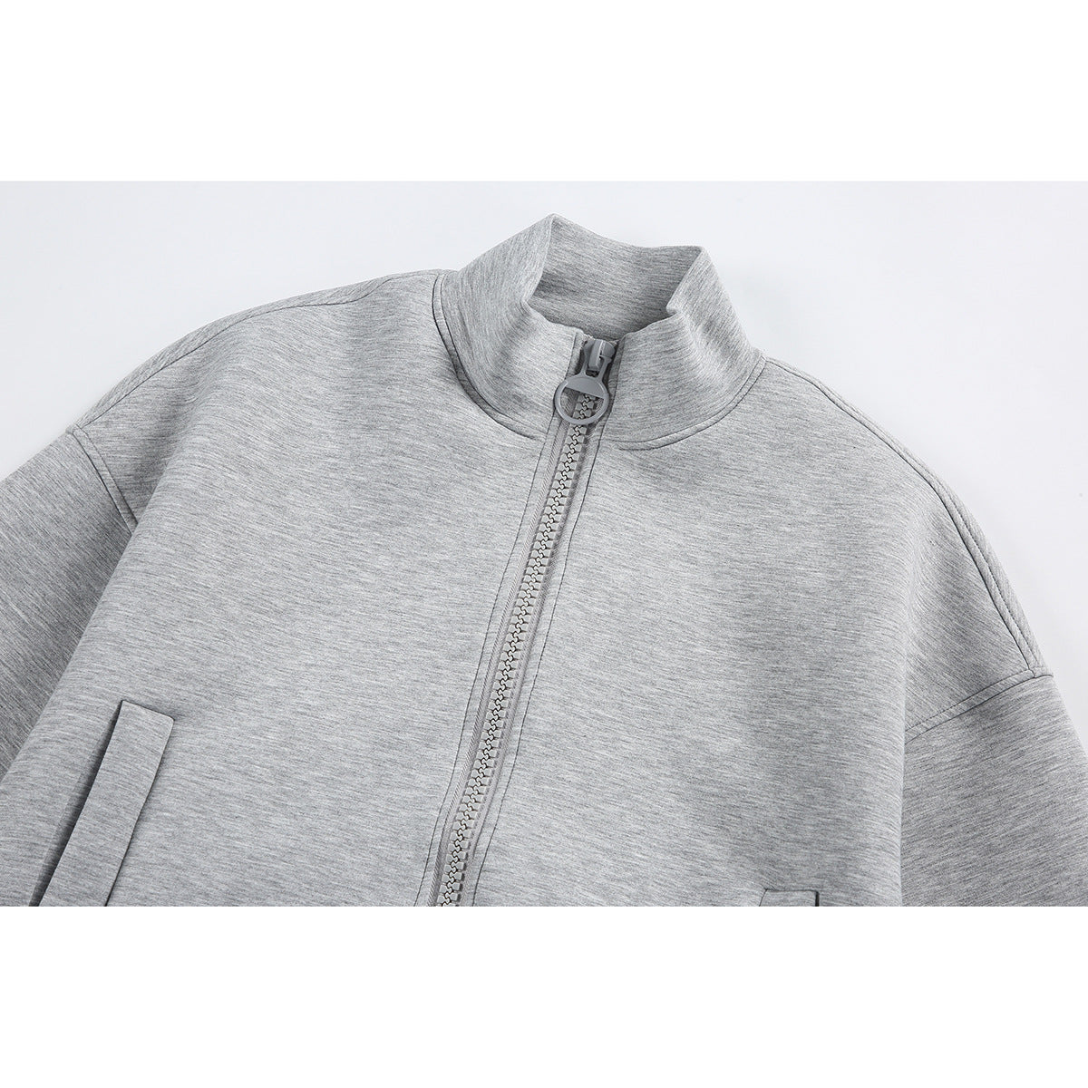 Close-up of a light gray zip-up jacket showing its stand collar, ring zipper pull, and front pockets.