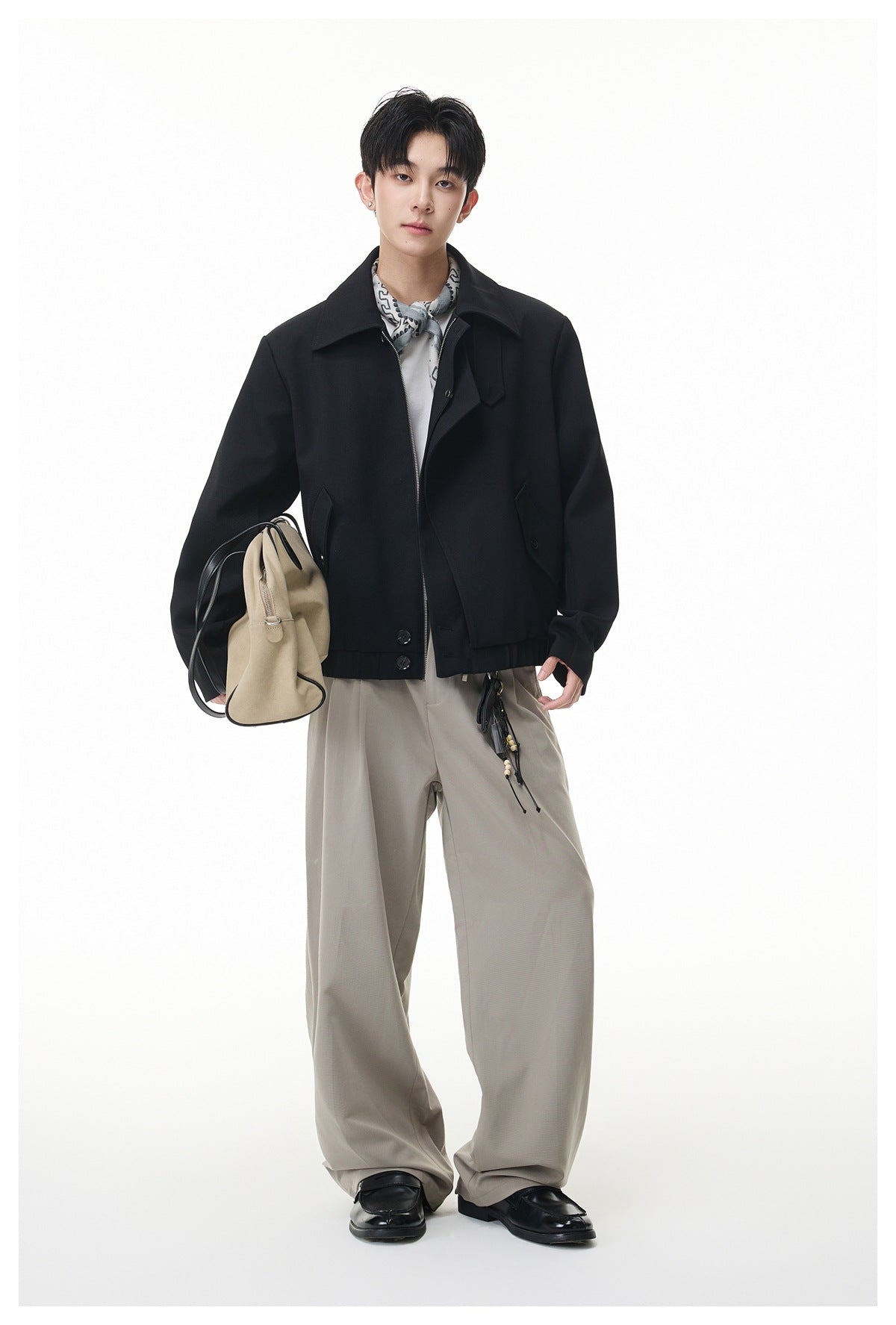 Model wearing a black zip-front jacket with beige wide-leg trousers, a patterned neck scarf, and black shoes.