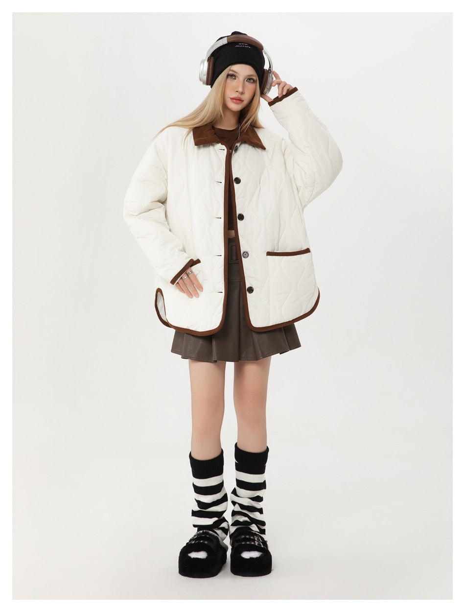 Model wearing off-white quilted jacket with brown trim, open over a brown top and pleated skirt, one hand raised