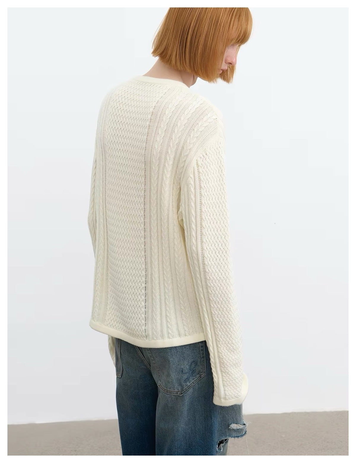 Model in a cream cable-knit sweater, shown from a rear three-quarter angle with blue jeans.