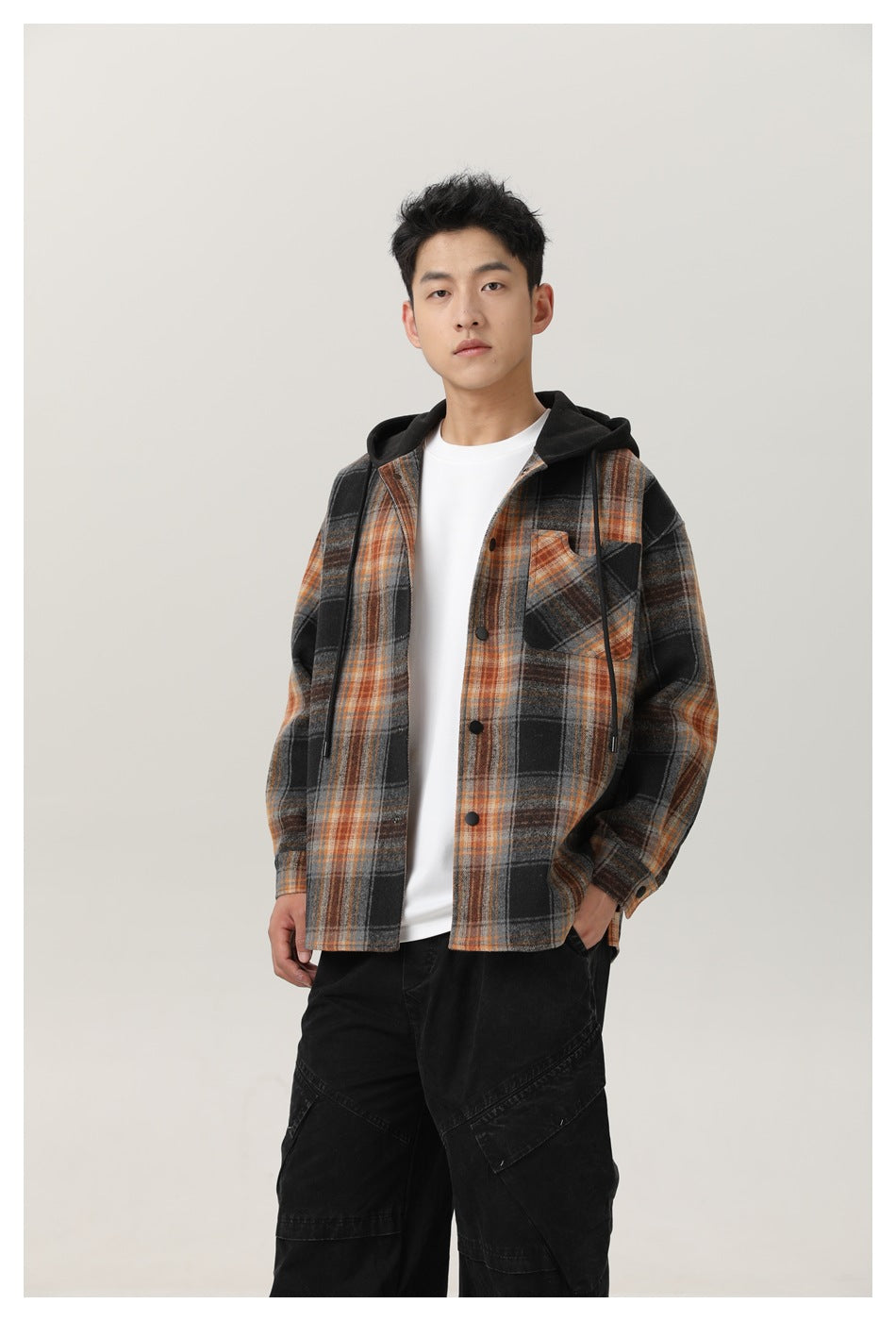 Man modeling a black, gray, and orange plaid button-front hooded overshirt with a chest pocket.