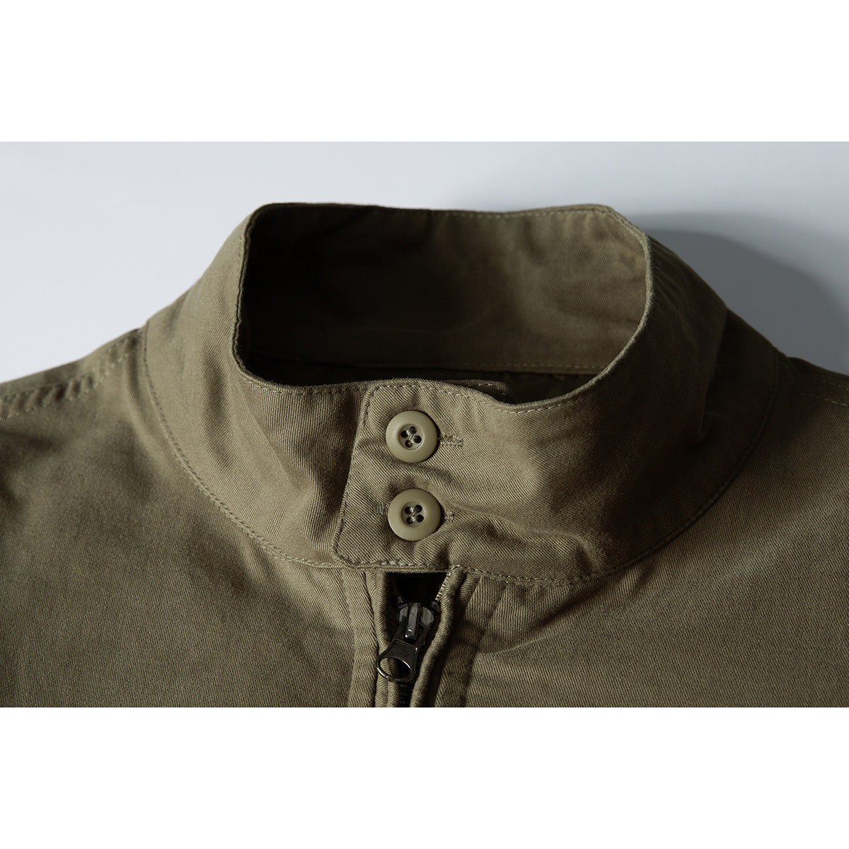 Close-up of an olive jacket's stand collar, two buttons, and front zipper.