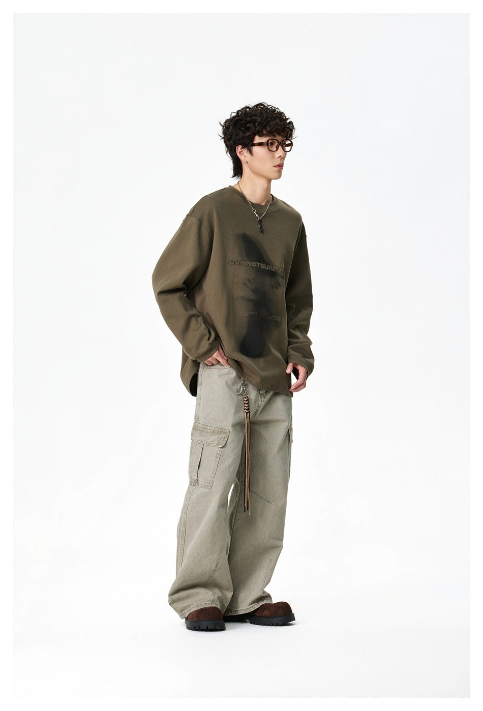 Side view of a model wearing an olive oversized graphic sweatshirt and loose light cargo pants.