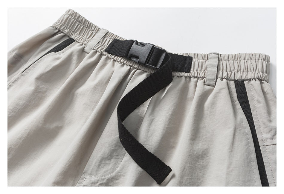 Close-up of the light gray shorts' gathered waistband, black buckle belt, and pocket trim.