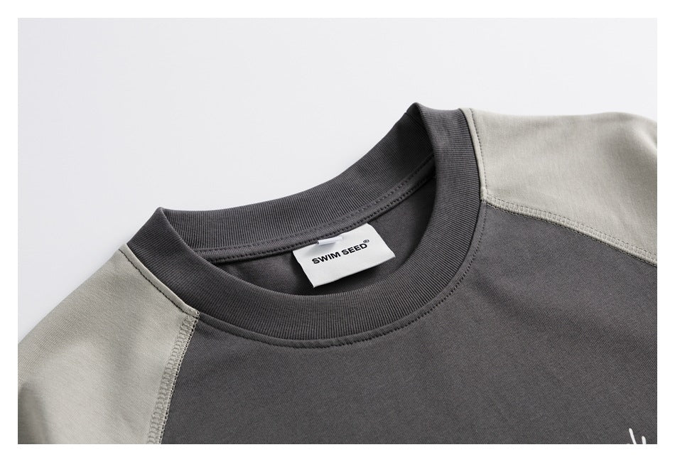 Close-up of a charcoal T-shirt's ribbed crew neck and light gray raglan shoulder seams, with a sewn neck label.