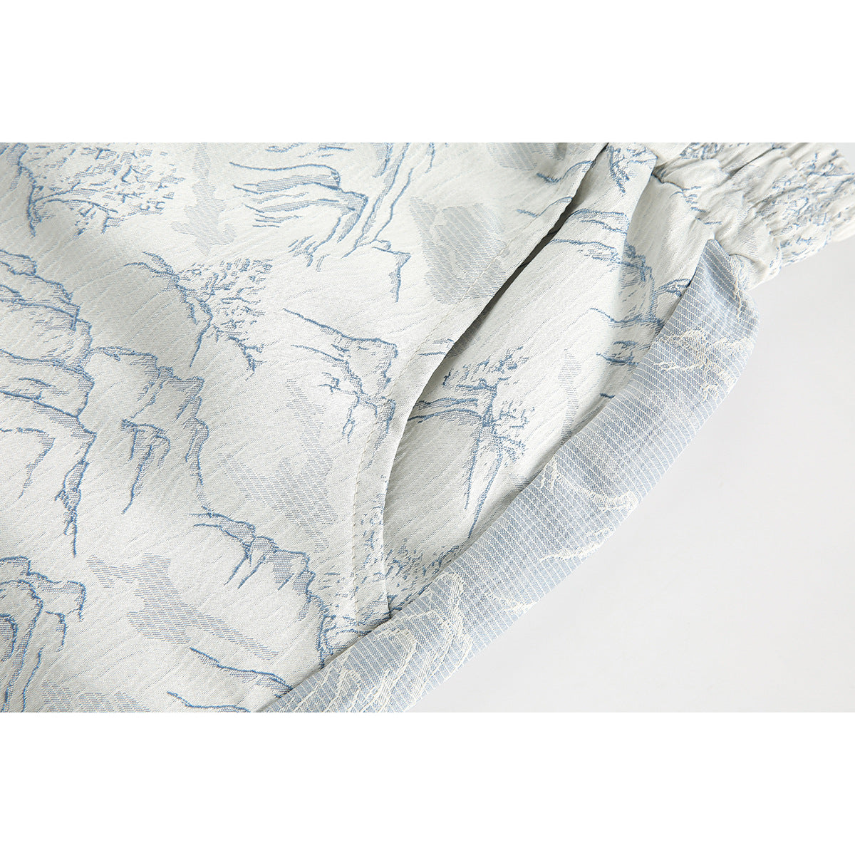 Close-up of the pale blue landscape print and folded seam on white shorts.