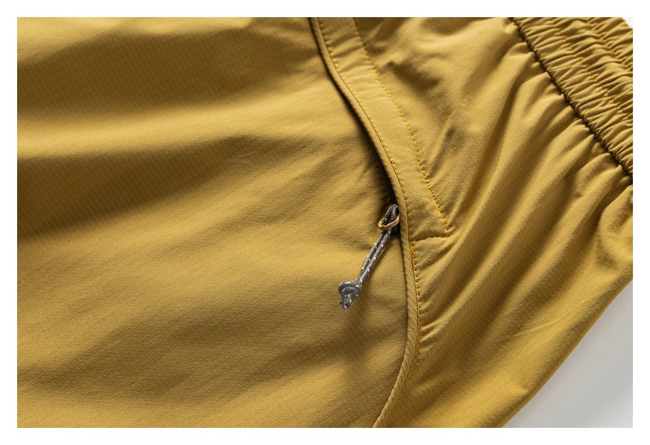 Close-up of mustard-gold trousers showing a pocket zipper pull beside the elastic waistband.