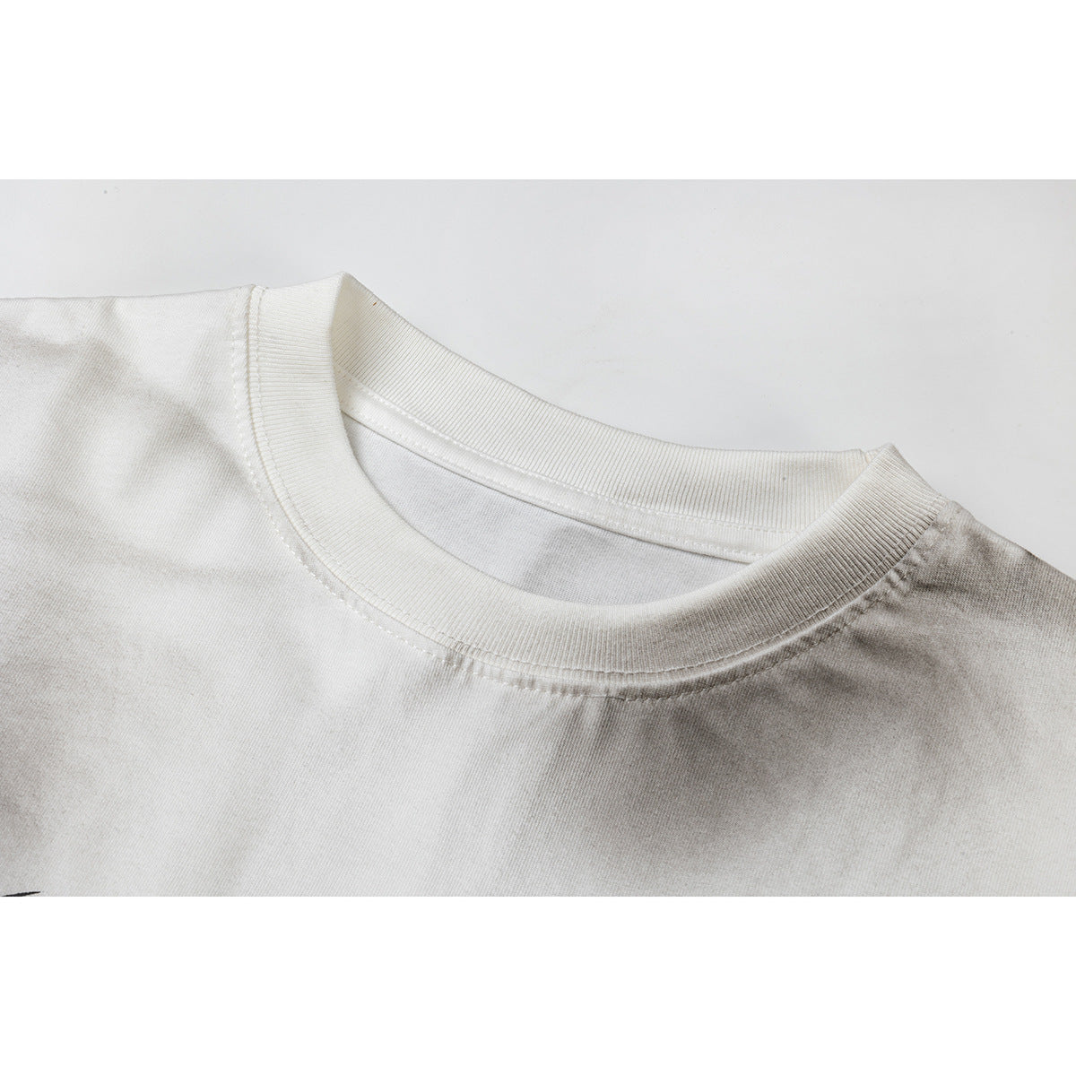 Close-up of the ribbed crew neckline and shoulder seam on a white T-shirt.