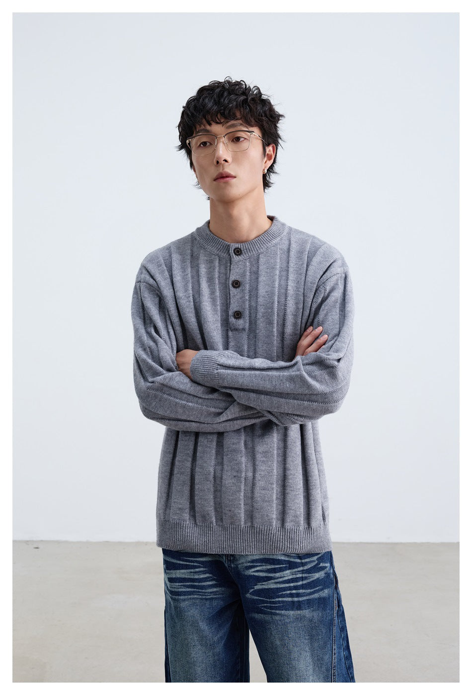 Model standing with arms crossed in a gray vertically paneled sweater with a three-button neck.