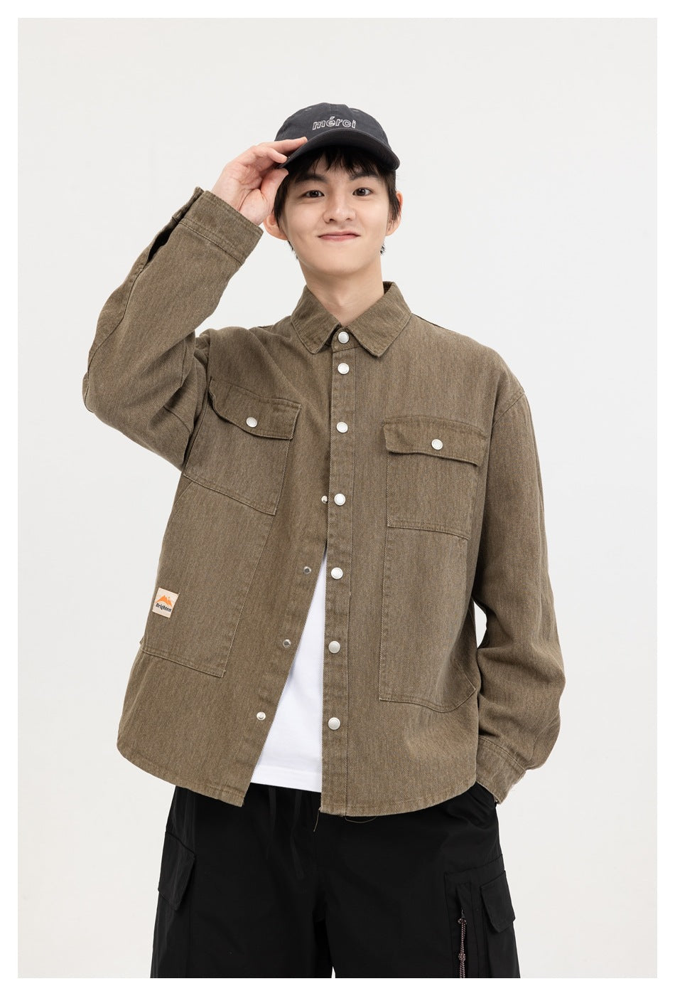 A smiling model wears a brown snap-front overshirt with two flap chest pockets, shown over a white shirt.