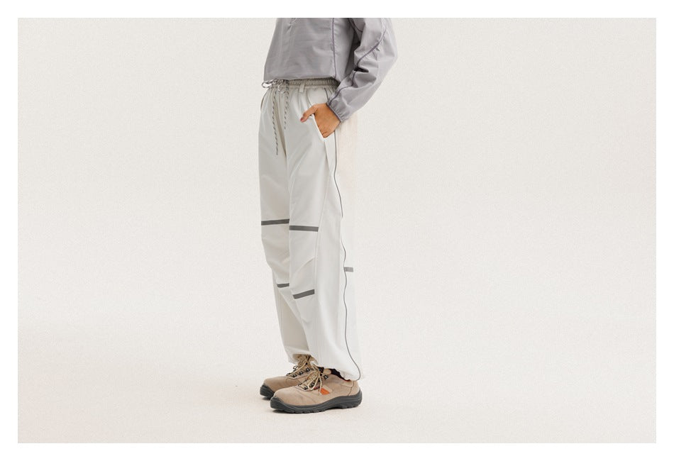 Cropped side view of a person wearing loose light-gray drawstring pants with dark reflective bands.