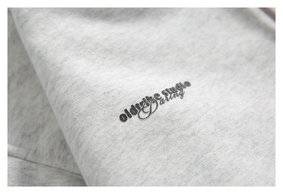 Close-up of a small dark raised logo on light gray heathered fabric.