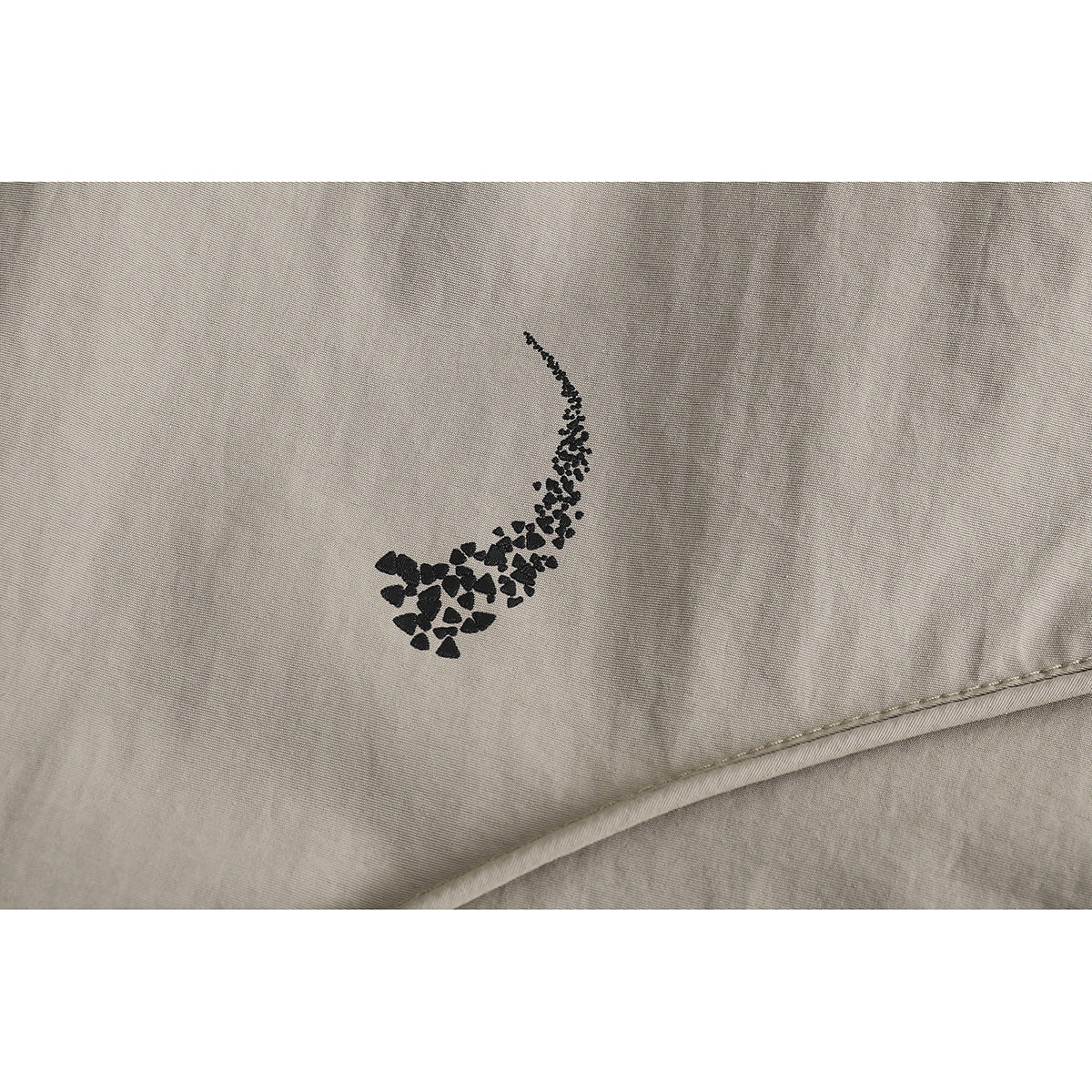 Close-up of taupe jacket fabric with a small black abstract printed motif and a diagonal seam.