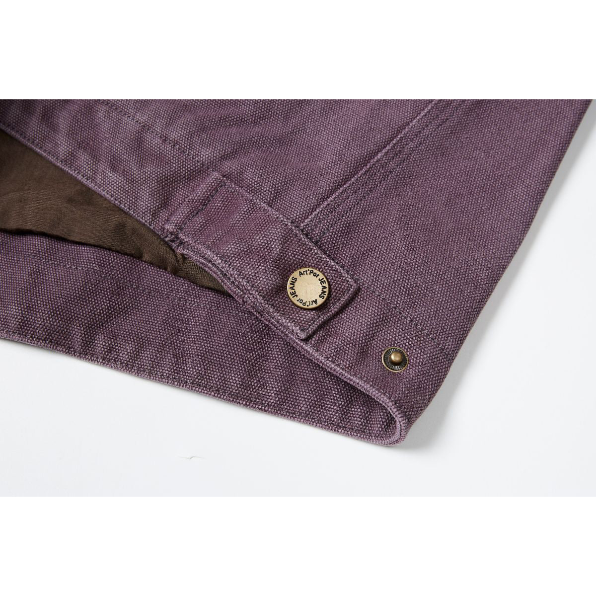 Close-up of the plum jacket's cuff tab, branded button, stitching, and metal snap.