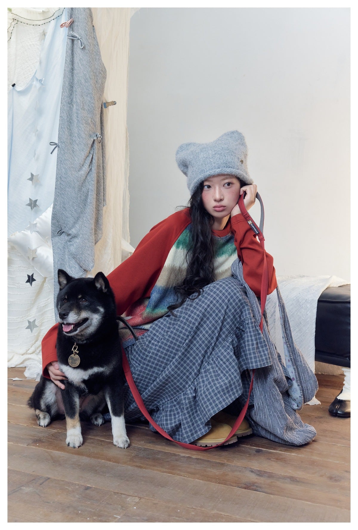 Model crouching beside a dog in a cream striped sweater with red sleeves and a blue plaid tiered skirt.