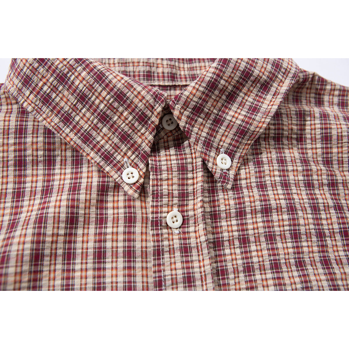 Close-up of a burgundy, rust, and cream plaid shirt collar with white buttons.