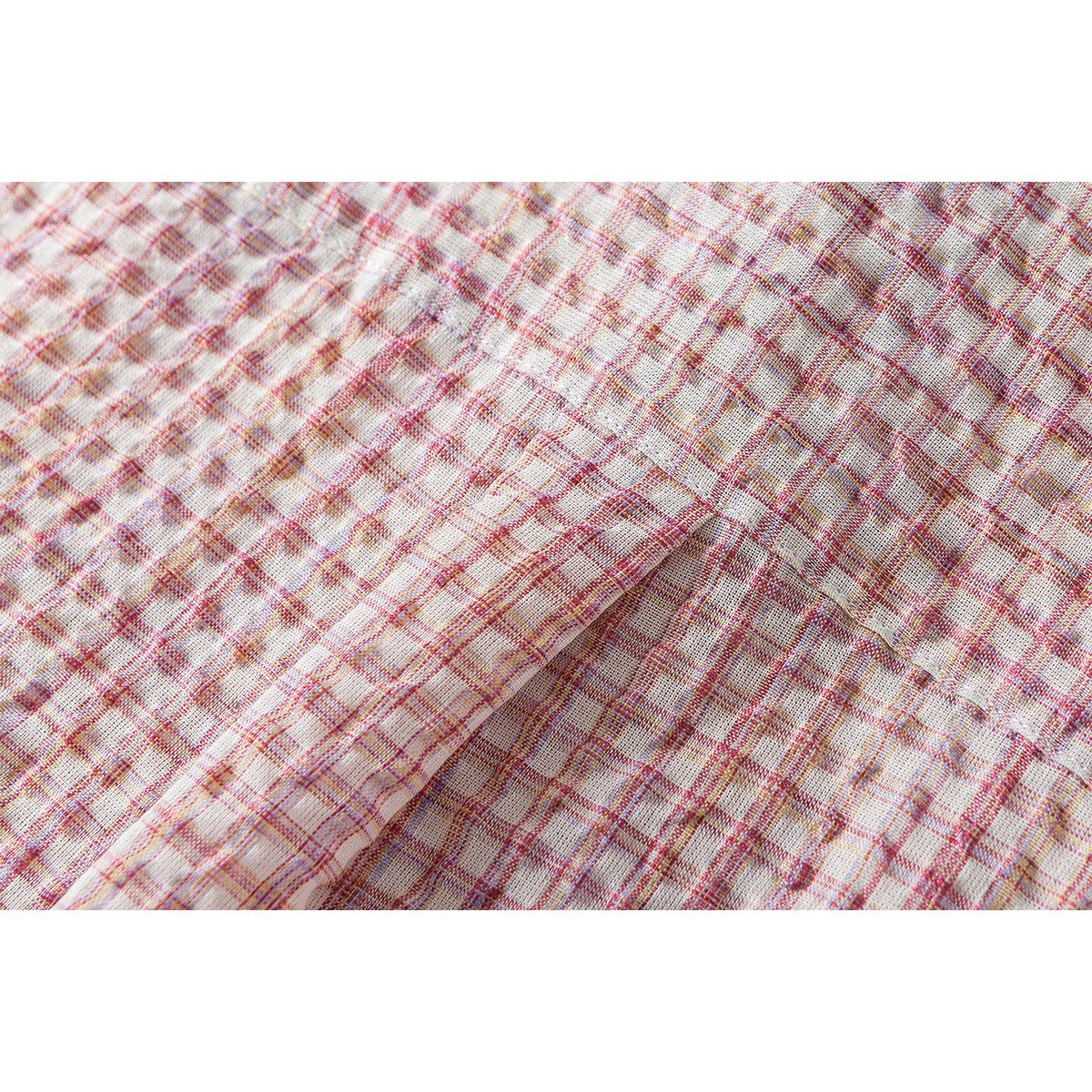 Macro view of the cream fabric's pink and muted gold plaid weave and stitching.