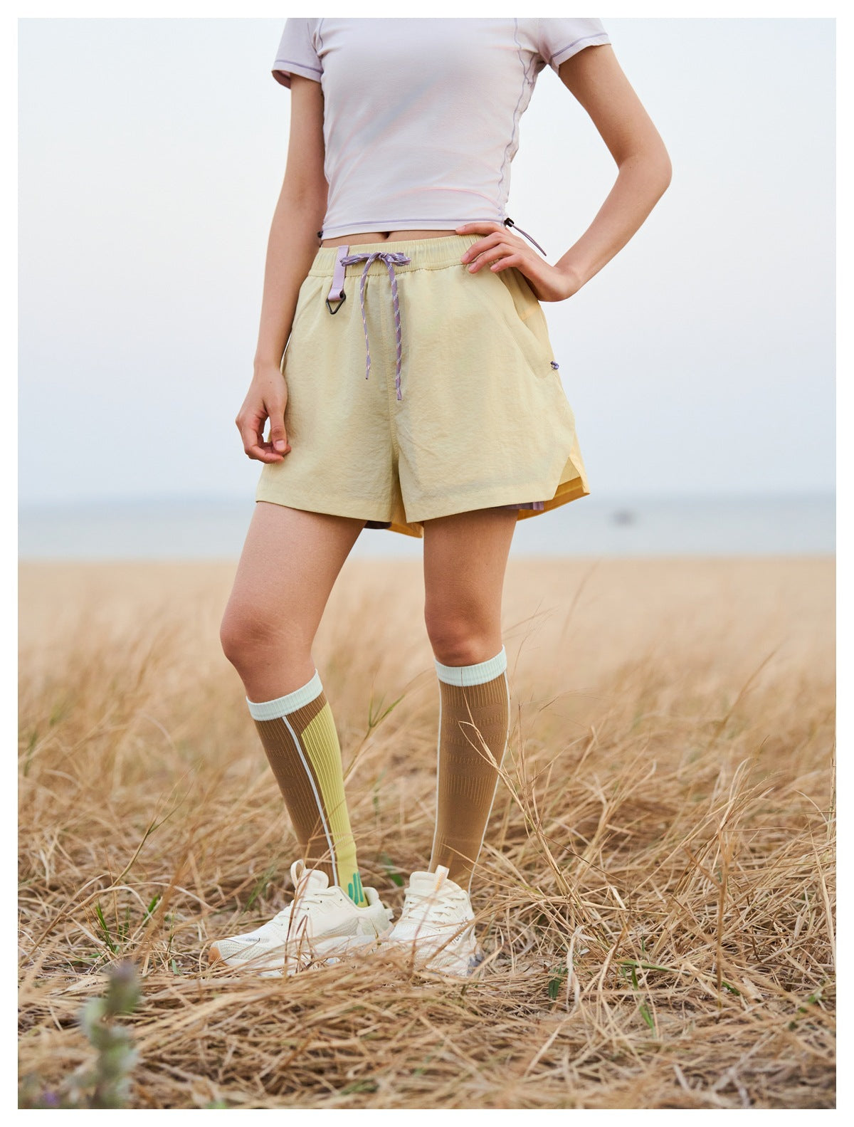 Close view of pale yellow shorts with an elastic waist, purple drawcord, and angled pockets.