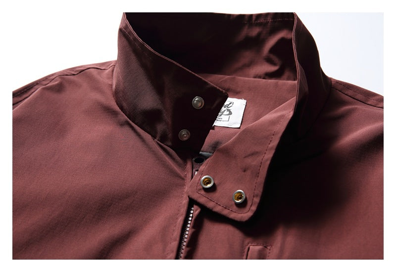 Close-up of a burgundy jacket's open stand collar, snap fasteners, and zipper.