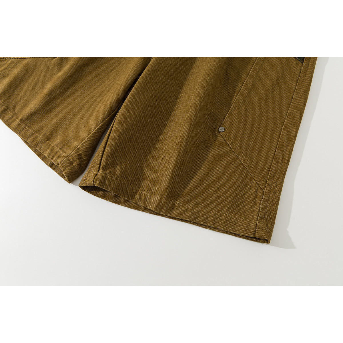 Close-up of mustard-brown shorts showing a wide hem and a small button on a side pocket seam.