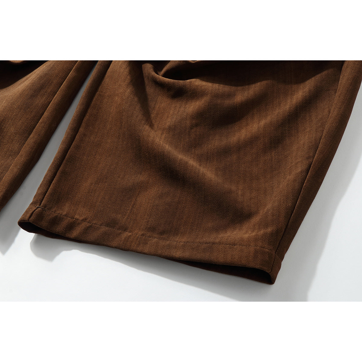 Close-up of the brown trouser legs and stitched hems laid flat.