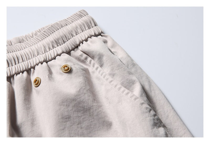 Close-up of pale gray shorts with a gathered elastic waistband, two tan buttons, and a diagonal pocket seam.