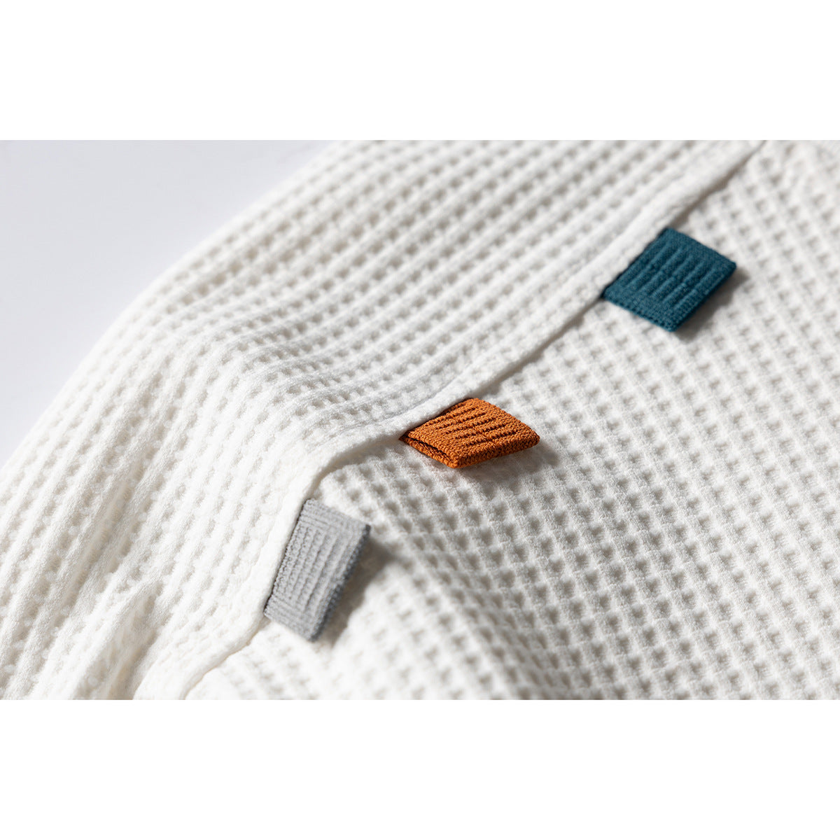 Close-up of an ivory waffle-textured shirt with small teal, rust, and gray fabric tabs.