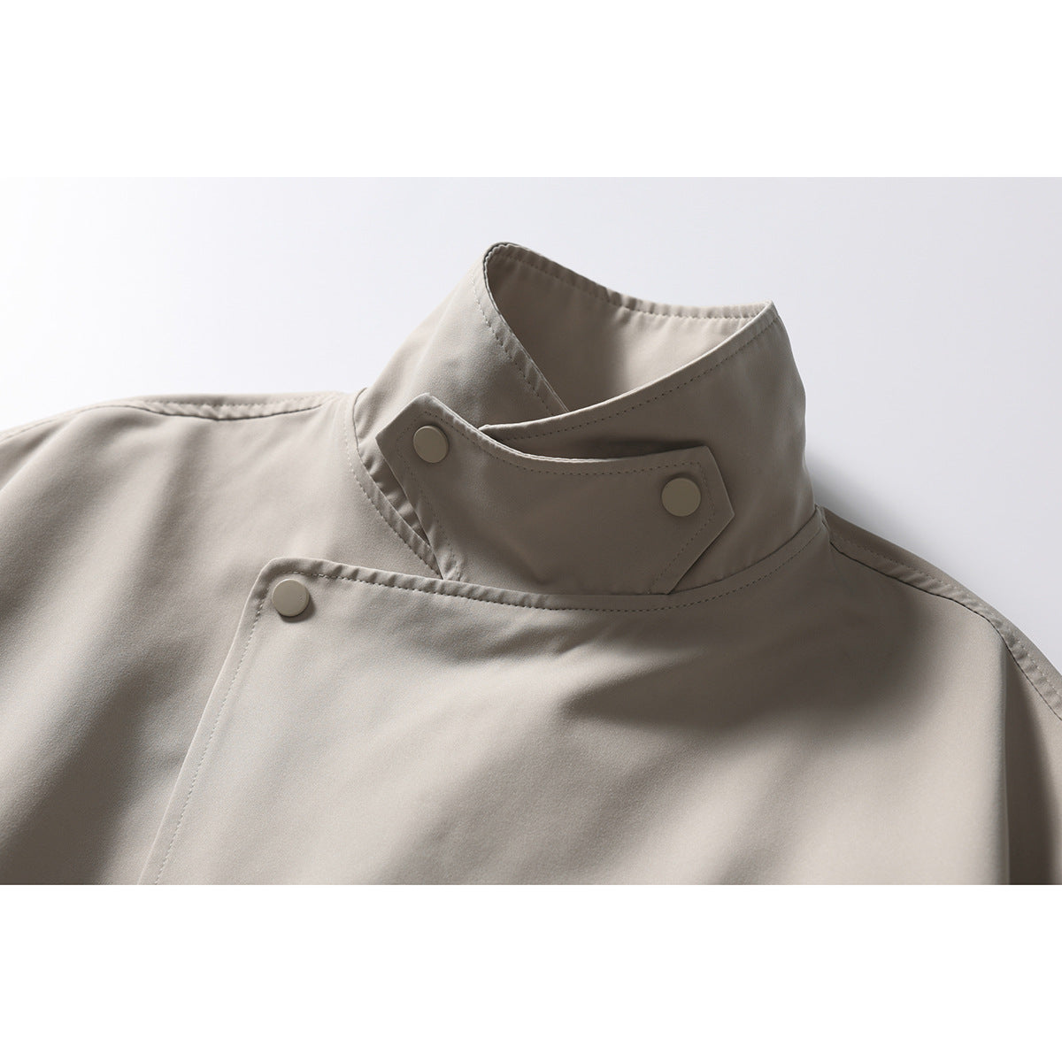 Close-up of a light taupe jacket’s high stand collar with overlapping snap-button tabs.