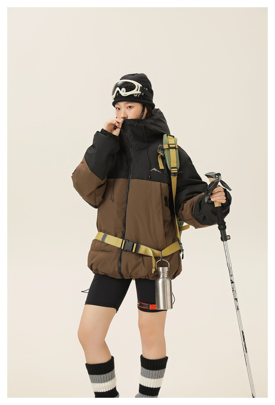 Model wearing a black-and-brown color-block hooded jacket with a yellow waist strap and backpack.