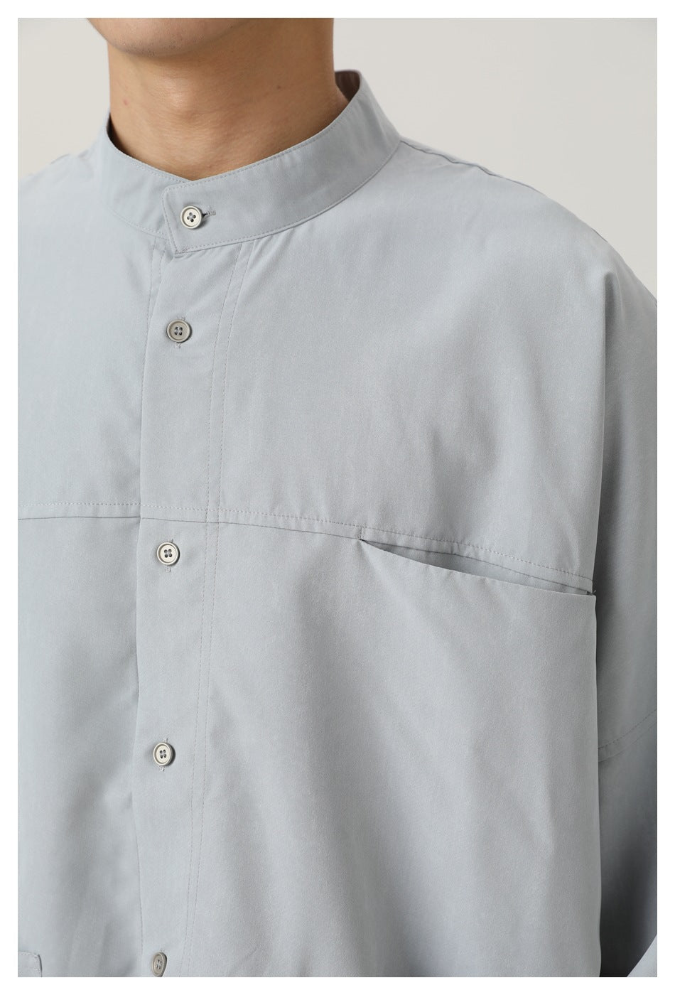 Close view of the light gray shirt's stand collar, button placket, chest seam, and angled chest pocket.