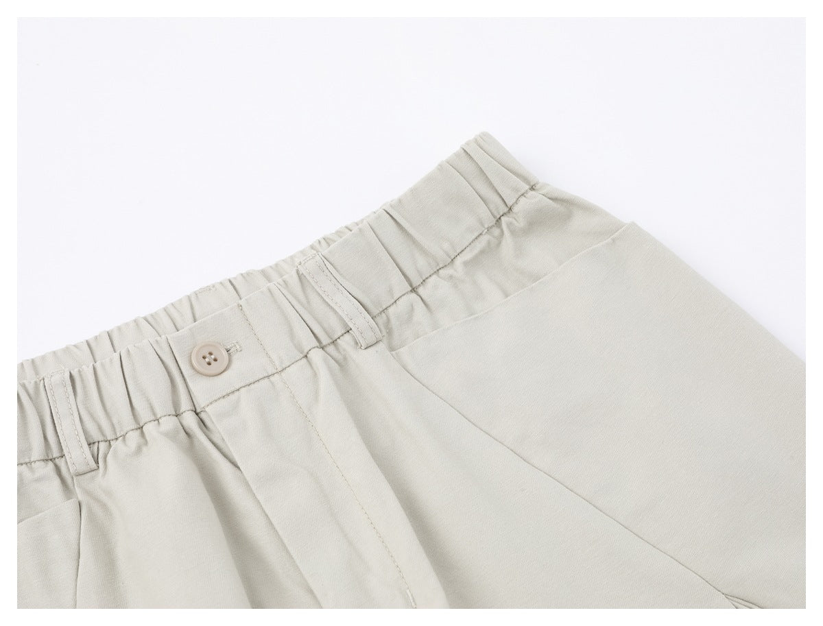 Close-up of the elastic waistband, button, belt loops and pocket seam on light ivory trousers.