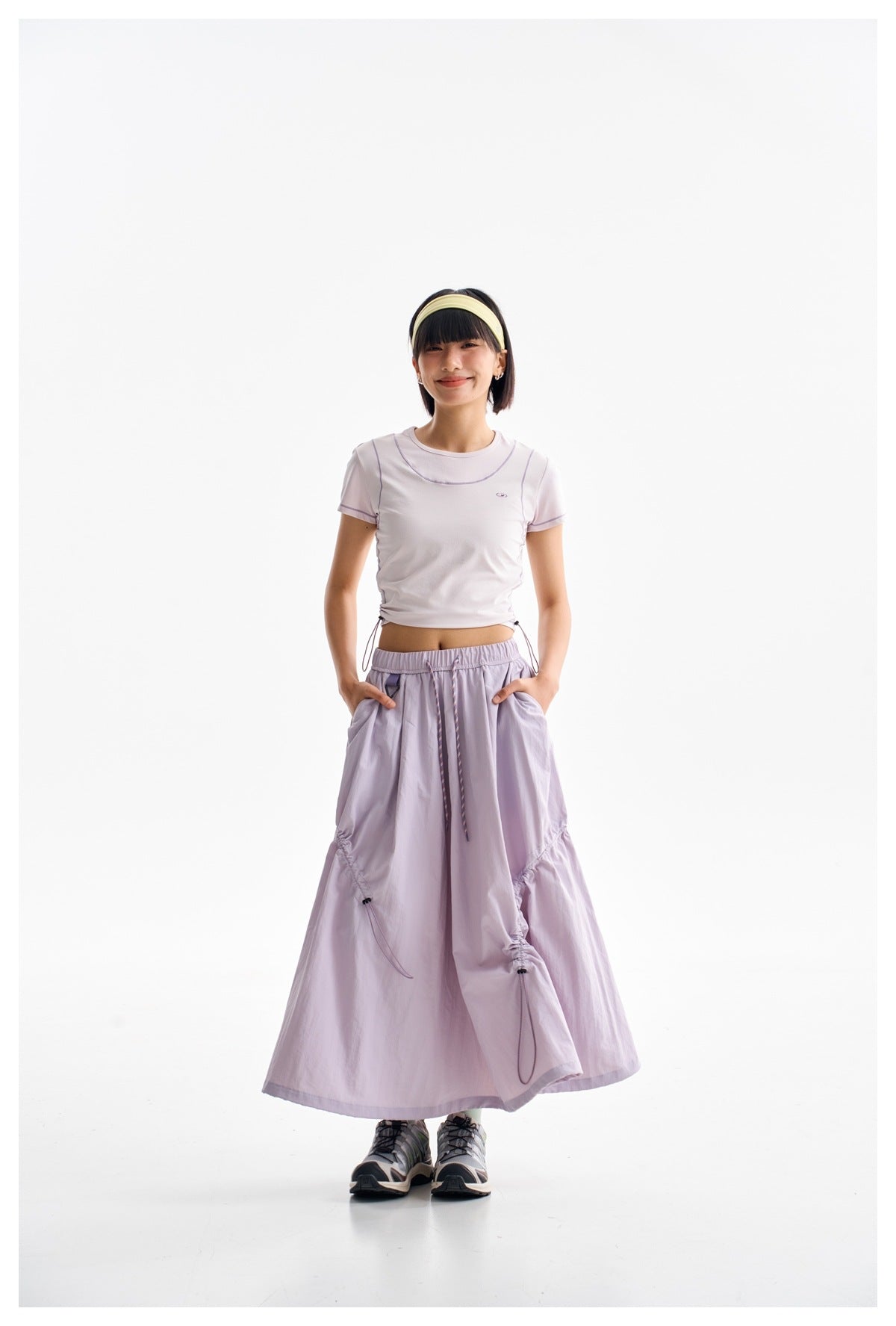 Front view of a model in a pale lilac cropped T-shirt and matching long gathered skirt with side drawcords.