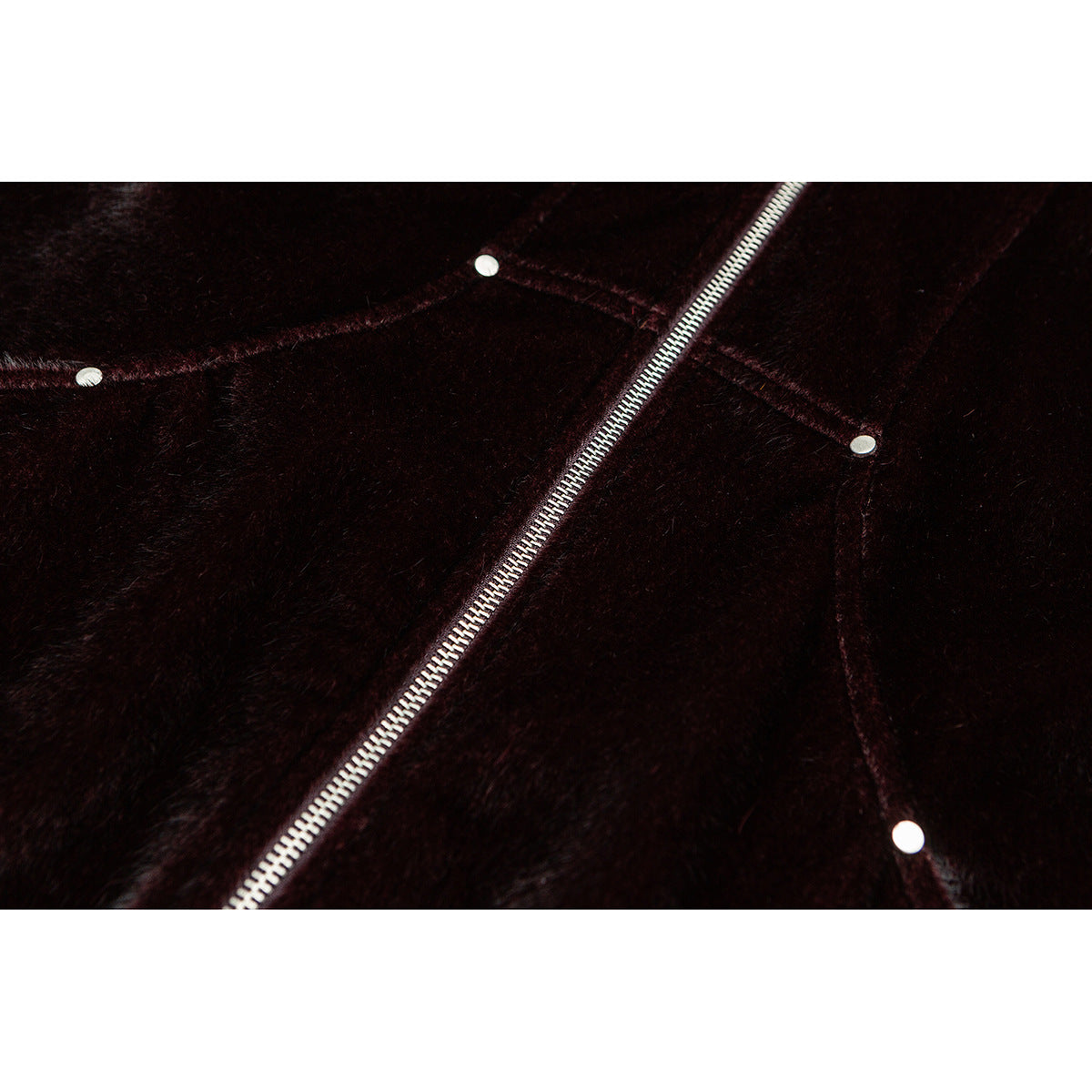 Close-up of a diagonal metal zipper and small round metal studs on dark burgundy-brown plush fabric.