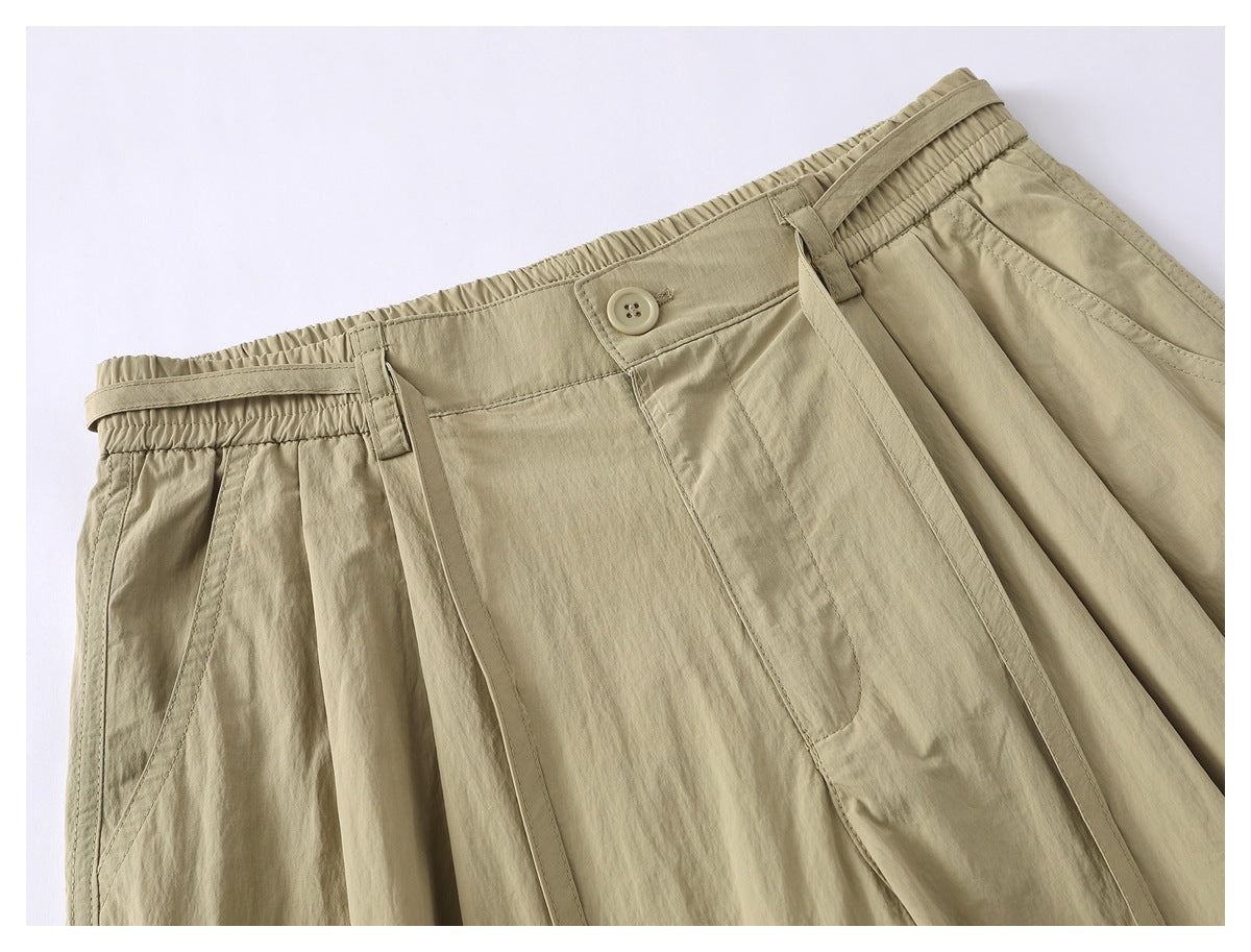 Close-up of beige shorts showing the elasticated waistband, button closure, belt loops, pleats and pocket opening.