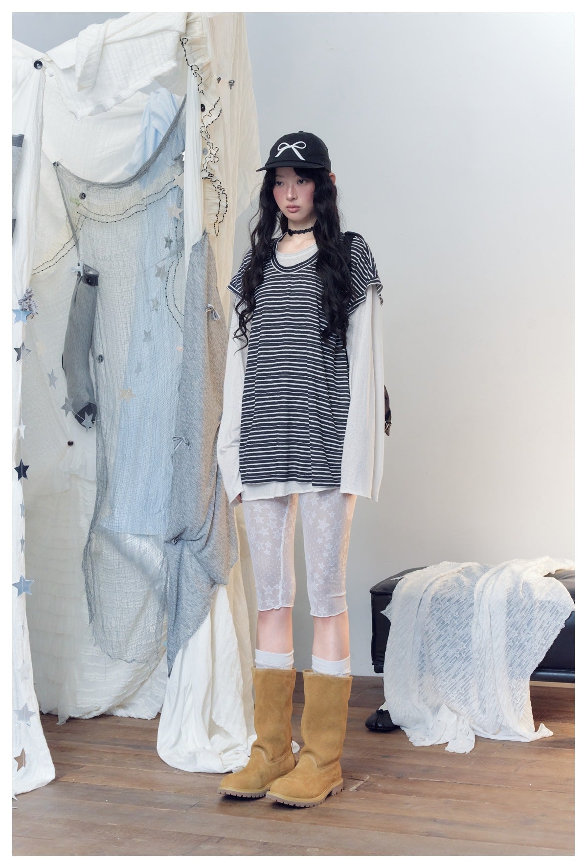 Model wearing a loose black-and-white striped short-sleeve top over a light long-sleeve shirt, with star-print capri