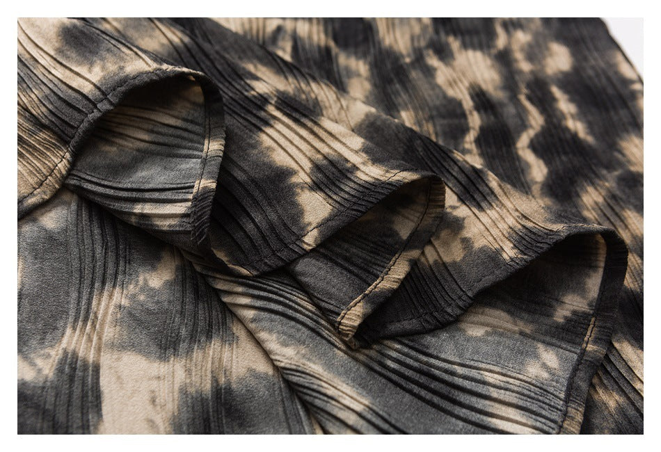 Close-up of several ruffled, pleated edges on a dark garment with a beige abstract print.