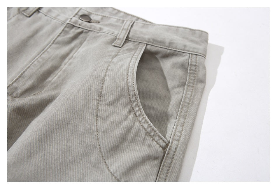 Close-up of light gray-beige trousers showing the front pocket, waistband, belt loop, and metal button.