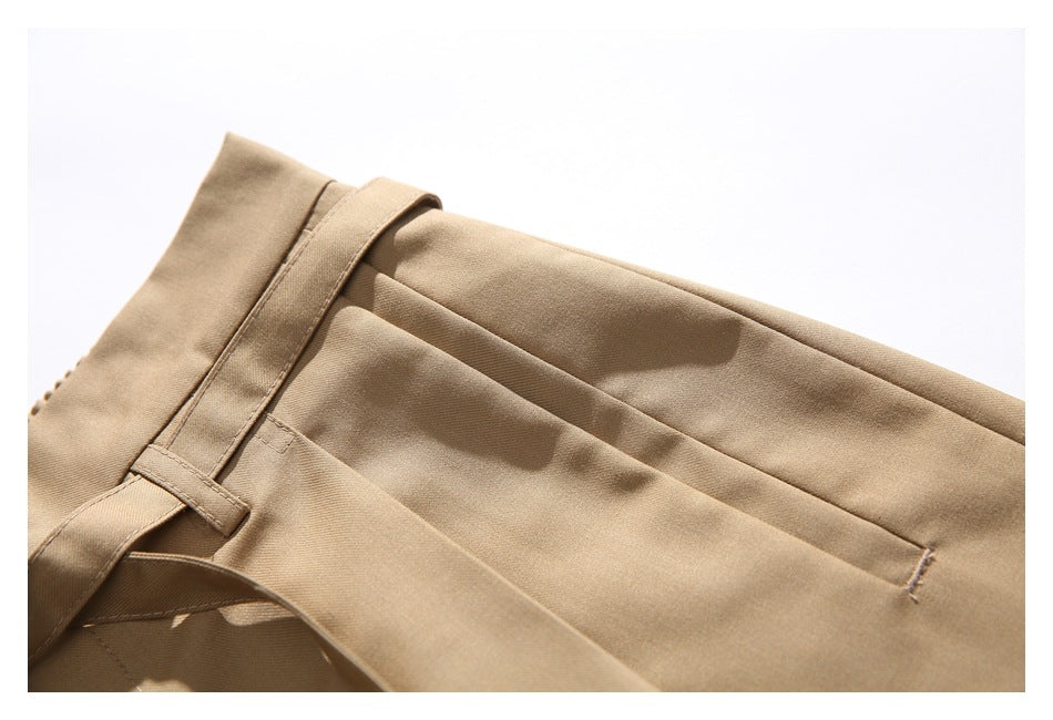 Close-up of tan trousers showing the waistband, belt loop, and front pleat.