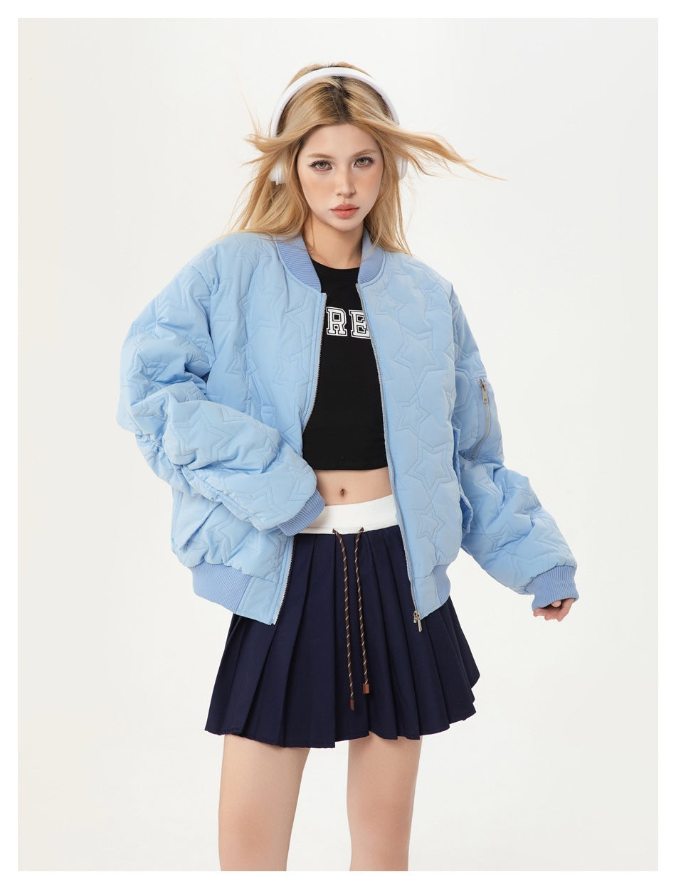 Model wearing an open pale blue star-quilted bomber jacket with a black cropped top and navy pleated skirt.