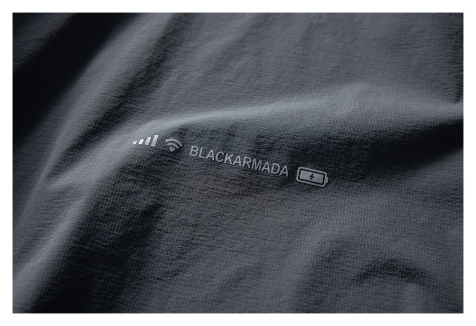 Close-up of dark gray garment fabric with printed BLACKARMADA text and small symbols.