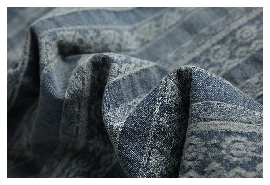 Close-up of folded blue-gray denim fabric with visible weave, stitching, and subtle woven patterns.