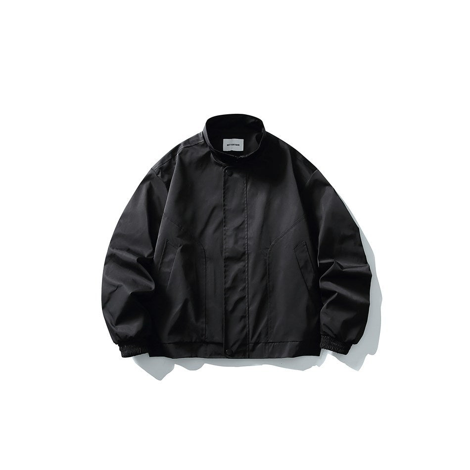 Black stand-collar jacket with snap placket, slanted front seams and elastic cuffs, flat lay on white