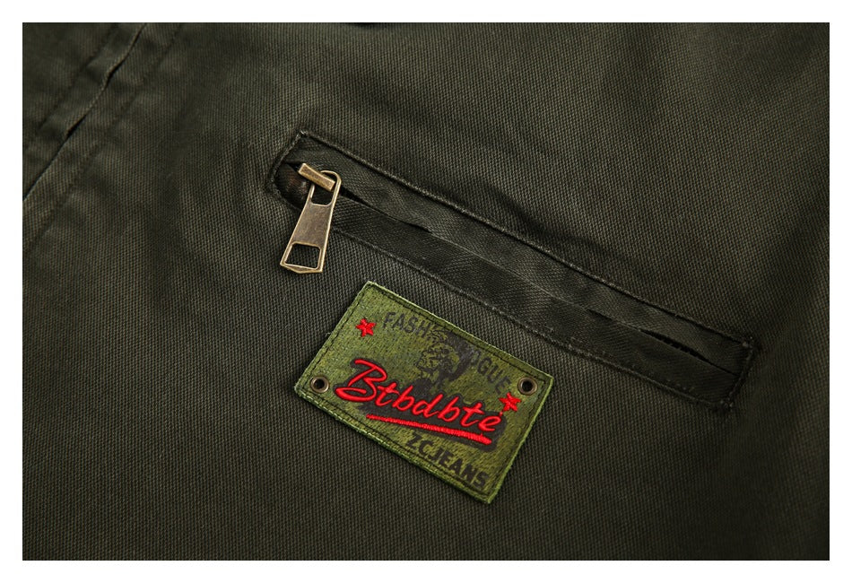 Close-up of an olive jacket with a diagonal zip pocket and a stitched green brand patch.