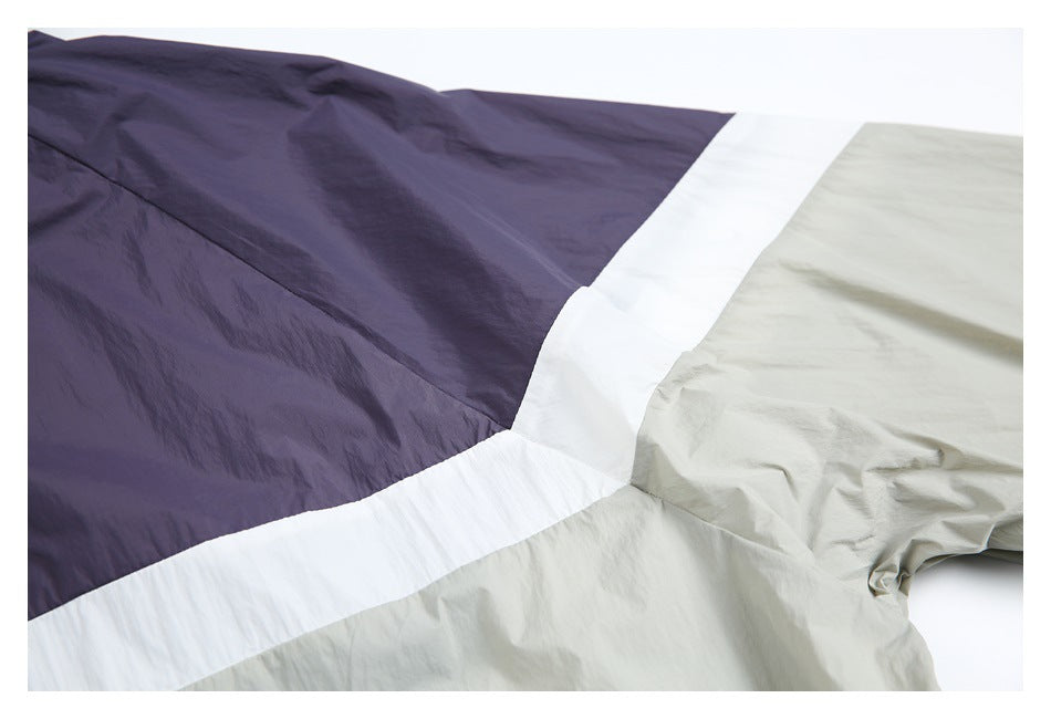 Close-up of the windbreaker’s purple, white, and light gray color-block panels and stitched seams.