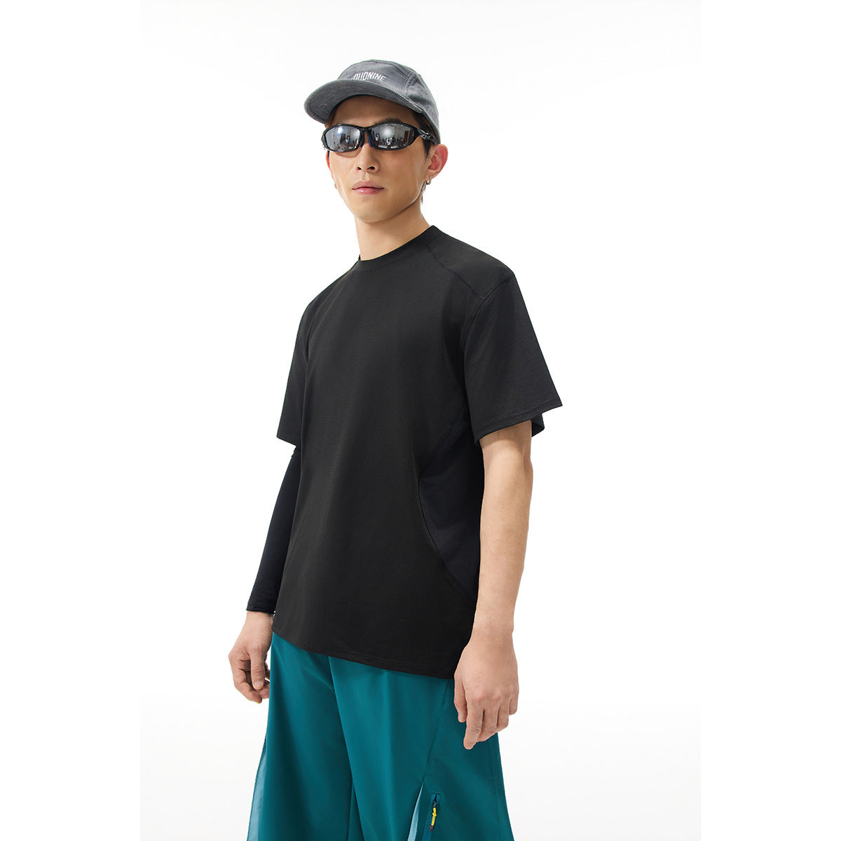 Model wearing a plain black short-sleeve T-shirt and teal shorts, shown from the front at an angle.