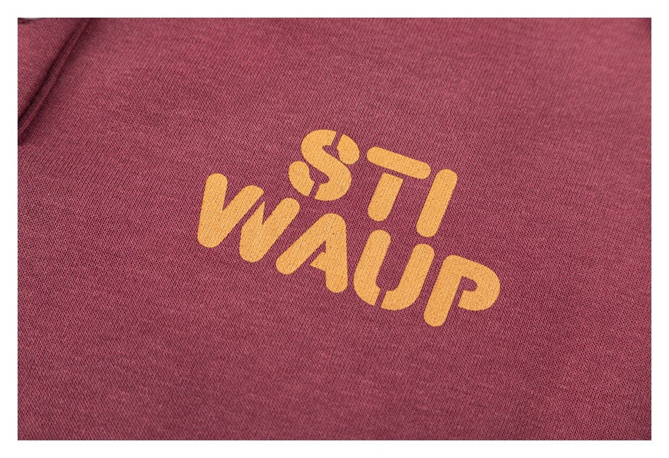 Close-up of yellow stylized lettering printed on the burgundy pullover.